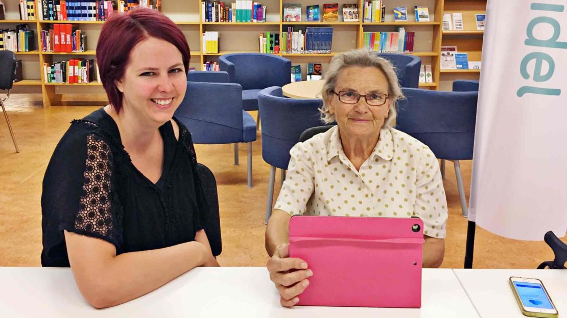 Gunilla Kvissberg, 90 år, får digital hjälp på biblioteket, här med Emelie Ekholm, handledare. Sin padda använder hon för att hålla kontakt med barn och barnbarn. Foto: Birgitta Hellman Magnusson.